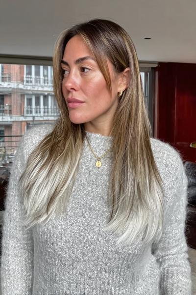 Eine Frau mit schulterlangem, glattem Haar trägt ein Balayage in Aschblond mit dunklem Ansatz und sanftem Farbverlauf zu helleren Spitzen.