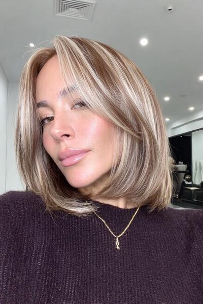 Eine Frau mit einem kinnlangen, glatten Bob trägt braun-blonde Haare mit hellblonden Highlights und Mittelscheitel.