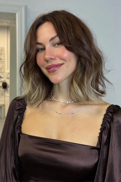 Eine Frau mit kinnlangem, welligem Haar in Braun mit blonden Spitzen (Balayage) und Mittelscheitel.