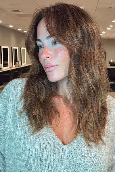Frau mit mittellangen, braun-blond balayage Haaren und sanften Wellen im modernen, lässigen Stil.