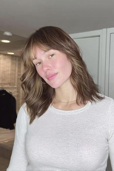 Eine Frau mit schulterlangem, welligem Haar in Braun mit blonden Highlights und Pony.