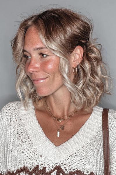 Eine Frau mit schulterlangem, welligem Haar in Braun-Blond-Balayage trägt einen natürlichen Look.