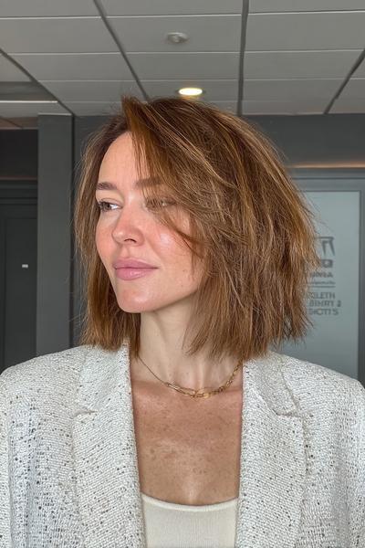 Eine Frau mit kinnlangem, stufig geschnittenem bronde Bob und seitlichem Scheitel.
