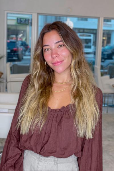 Eine Frau mit langen, welligen Haaren trägt einen natürlichen Balayage-Look mit blonden Strähnchen in den Spitzen und braunem Ansatz.