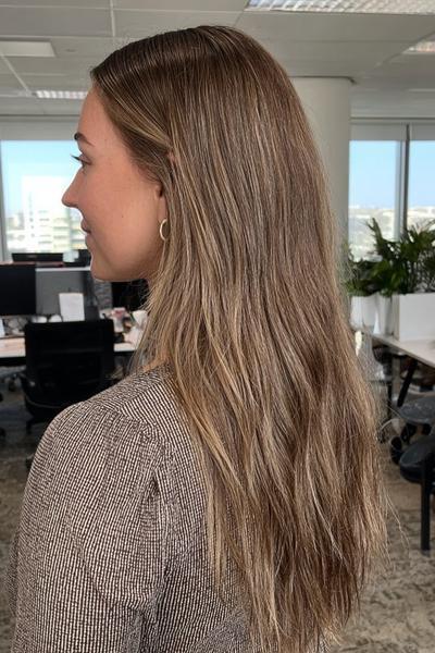 Frau mit langen, leicht gewellten braunen Haaren und dezenten blonden Strähnchen im Büro.