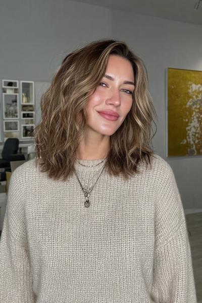 Frau mit schulterlangem, welligem dunkelblondem Haar und sanften Balayage-Highlights.
