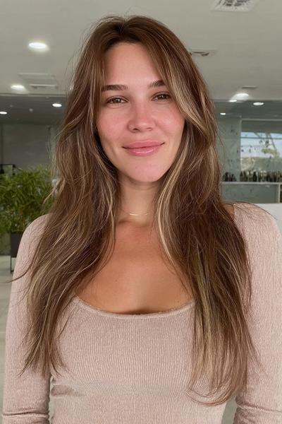 Eine Frau mit langen, braunen Haaren und dezenten, blonden Strähnchen im Balayage-Stil.
