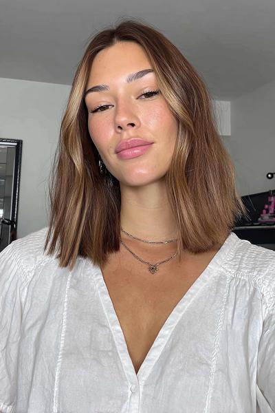 Frau mit schulterlangem, braunem Haar und dezenten, blonden Highlights im Mittel-Scheitel-Look.