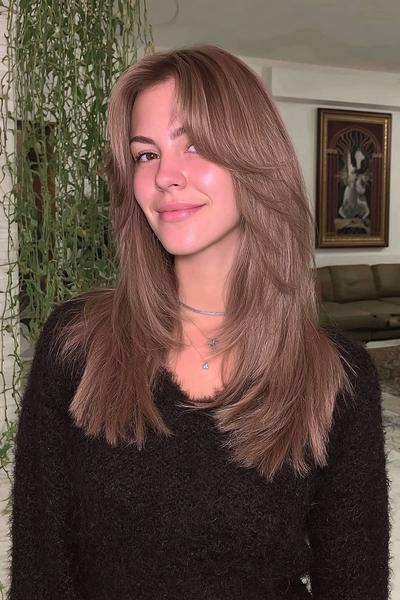 Eine Frau mit dunkelblondem, glattem Haar trägt eine stufig geschnittene Frisur mit sanften Curtain Bangs.