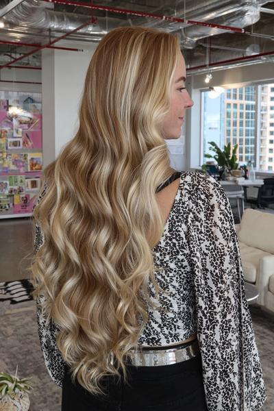 Eine Frau mit langen, welligen Haaren trägt natürliche blonde Strähnchen in einem modernen Balayage-Stil.