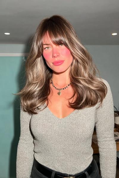 Frau mit mittellangem, welligem Haar im Braun-Blond-Balayage-Stil und locker fallendem Pony.