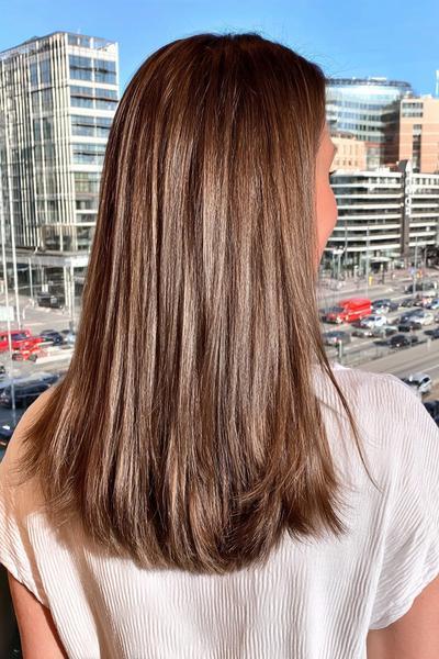 Eine Frau mit glatten, schulterlangen, dunkelblonden Haaren steht vor einer modernen Stadtlandschaft.