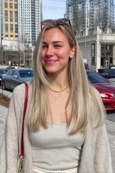 Eine junge Frau trägt glattes, langes Haar in einem natürlichen Aschblond-Balayage-Stil.