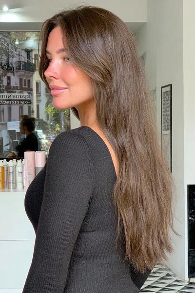 Eine Frau mit langen, glatten braun-blonden Haaren trägt einen Mittelscheitel und ihr Haar fällt natürlich über die Schultern und den Rücken.