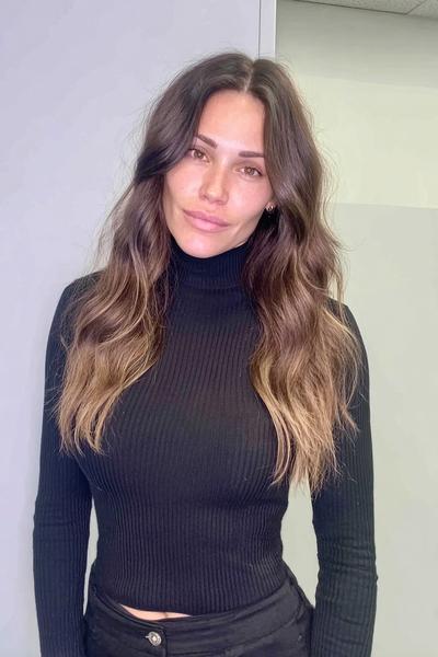 Eine Frau mit langem, dunkelblondem Haar, das in sanften Wellen gestylt ist und dezente, hellere Spitzen aufweist.