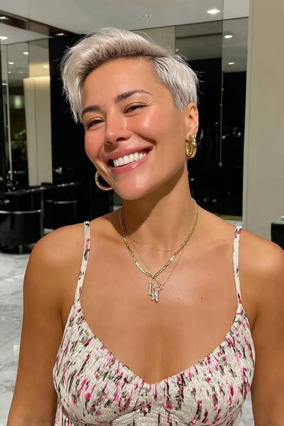 Eine Frau mit einem modernen, sehr kurzen, platinblonden Pixie Cut und seitlich gestyltem Pony lächelt in die Kamera.