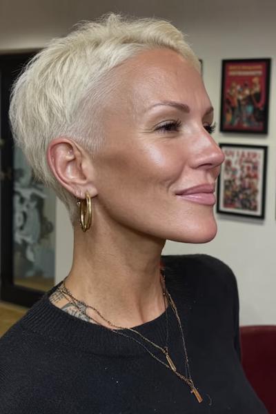 Eine Frau mit einem sehr kurzen, platinblonden Pixie Cut, bei dem die Seiten und der Hinterkopf knapp rasiert sind.
