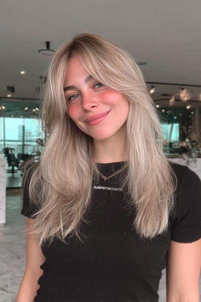 Eine Frau mit dunkelblonden, mittellangen Haaren und sanften Stufen trägt einen natürlichen, glatten Look mit Pony.
