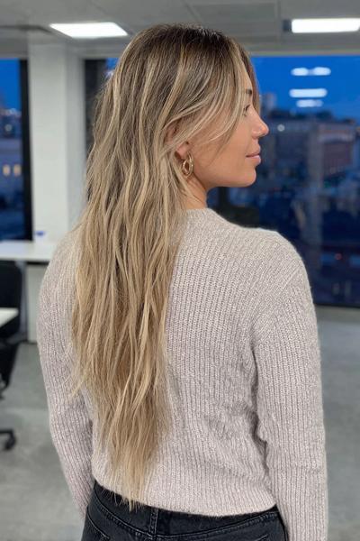 Eine Frau mit langen, welligen Haaren trägt blonde Strähnchen, die sanft in ihr dunkleres Haar übergehen.