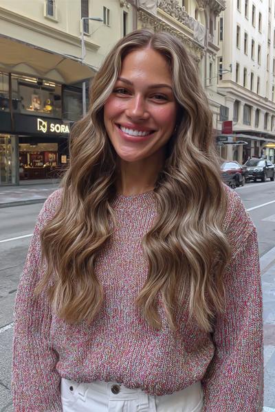 Eine Frau mit langen, welligen Haaren trägt ein Balayage in aschblonden Tönen.