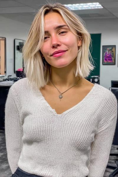 Eine Frau mit kinnlangem, welligem Haar im aschblonden Balayage-Stil steht in einem Friseursalon.