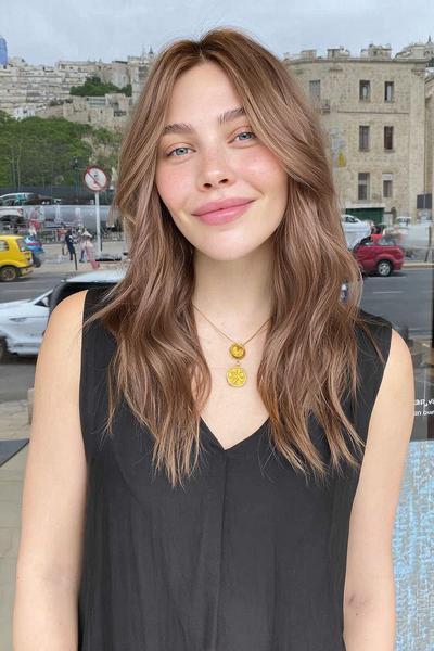 Eine Frau mit langen, gewellten, braunen Haaren hat feine, natürliche blonde Strähnchen, die dem Haar einen dezenten Glanz verleihen.