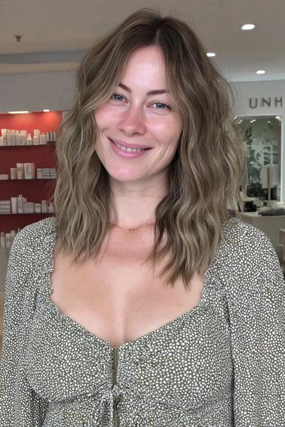 Eine Frau mit schulterlangem, welligem Haar trägt ein aschblondes Balayage in natürlichen, kühlen Tönen.