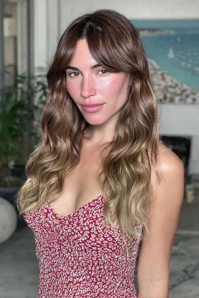 Eine Frau mit langen, welligen Haaren trägt einen aschblonden Balayage-Stil, bei dem die Haarspitzen heller sind als der Ansatz.