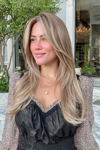 Eine Frau mit langen, glatten Haaren im aschblonden Balayage-Stil, deren Haar sanft gestuft und mittig gescheitelt ist.