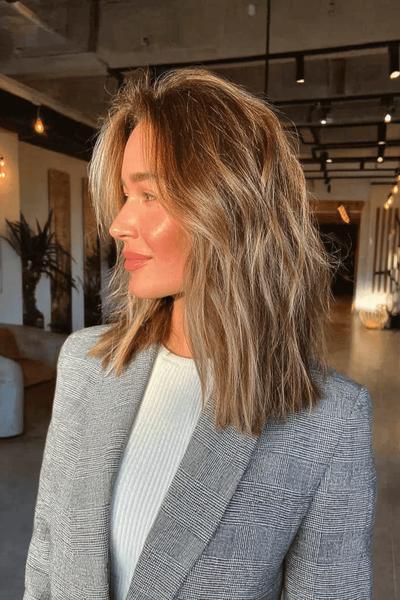 Frau mit schulterlangem, welligem Haar und dezenten blonden Strähnchen in einem natürlichen Balayage-Look.