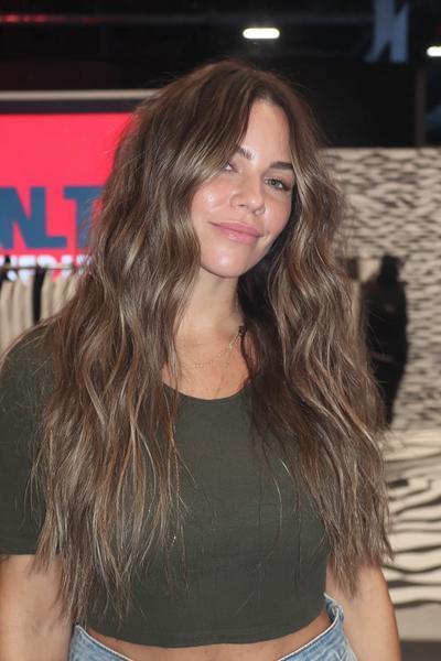 Eine Frau trägt langes, welliges braun-blondes Haar mit sanften Balayage-Highlights und Mittelscheitel.