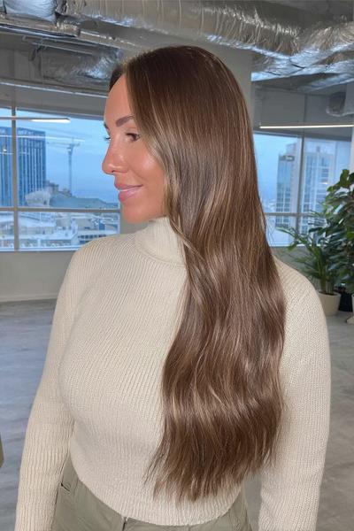 Frau mit langen, welligen Haaren in einem natürlichen Braun-Blond-Ton, seitlich gescheitelt und glatt fallend.