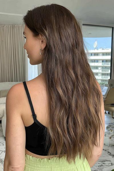 Frau mit langen, welligen Haaren in einem natürlichen Braunton mit dezenten blonden Highlights.