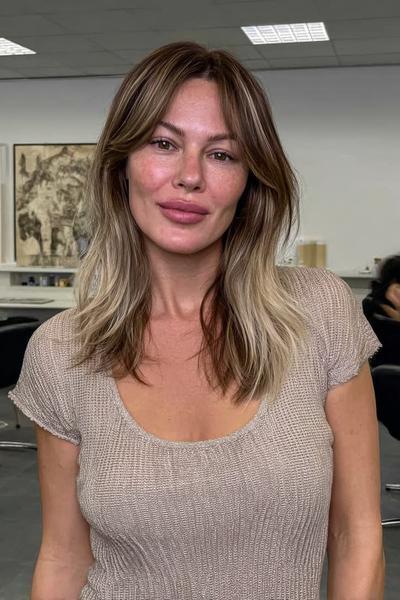 Eine Frau mit mittellangem, dunkelblondem Haar trägt einen Balayage-Stil mit aschblonden Spitzen.
