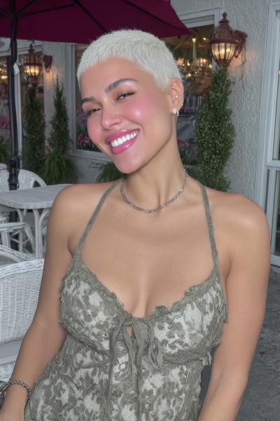 Eine Frau mit einem sehr kurzen, platinblonden Pixie-Cut und glattem Styling lächelt in die Kamera.