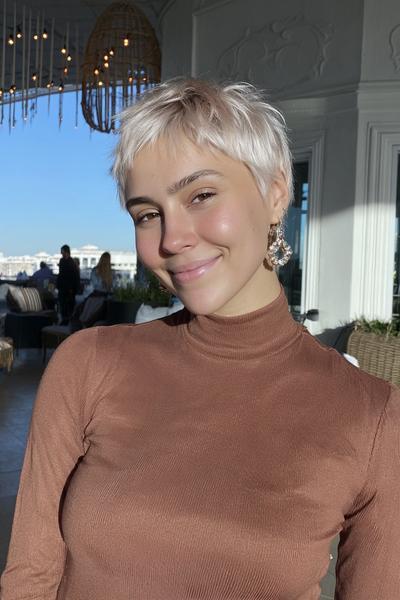 Eine Frau mit einem modernen, platinblonden Pixie-Cut, der leicht zerzaust und mit seitlichem Pony gestylt ist.