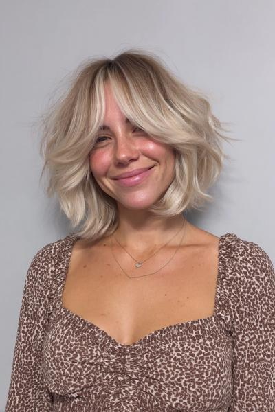 Eine Frau mit einem kinnlangen, welligen Bob und einem Balayage in Aschblond mit dunkleren Ansätzen und helleren Spitzen.