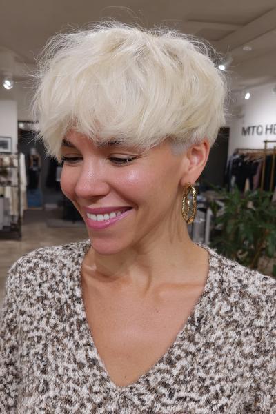Eine Frau mit einem voluminösen, platinblonden Pixie Cut mit fransigem Pony und seitlich kürzeren Haaren lächelt.