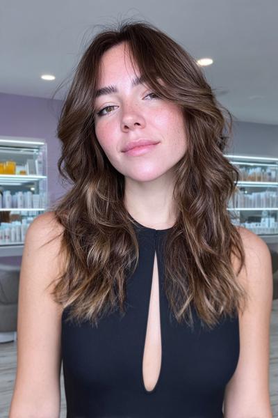 Frau mit mittellangem, welligem Haar in einem Braun-Blond-Balayage-Stil und sanftem Stufenschnitt.