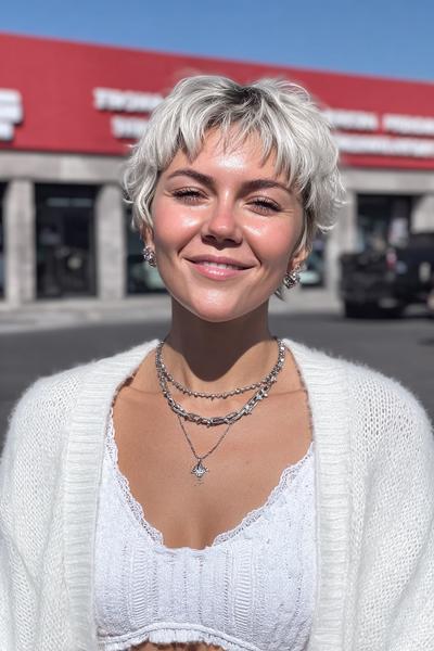 Eine junge Frau trägt einen kurzen, welligen, platinblonden Pixie Cut mit fransigem Pony.